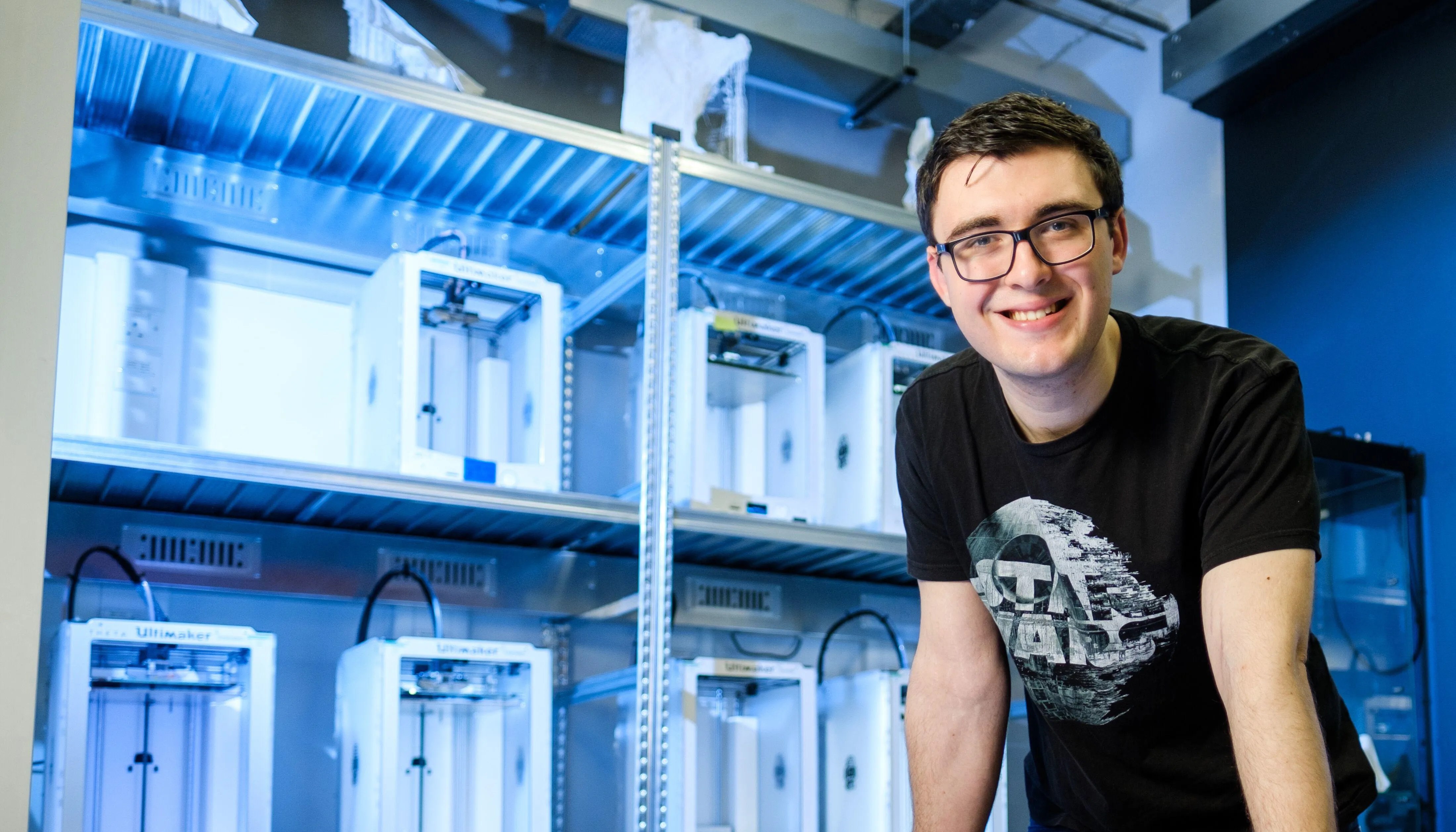 A male Computer Science student standing at a desk in a lab