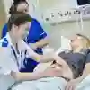 A smiling midwifery student in white NHS uniform examines a pregnant woman while a supervisor watches on