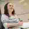 A female maths student in a white jumper laughing while writing in a notebook
