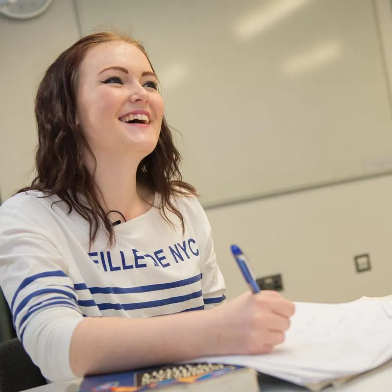 A student smiles whilst writing on paper.