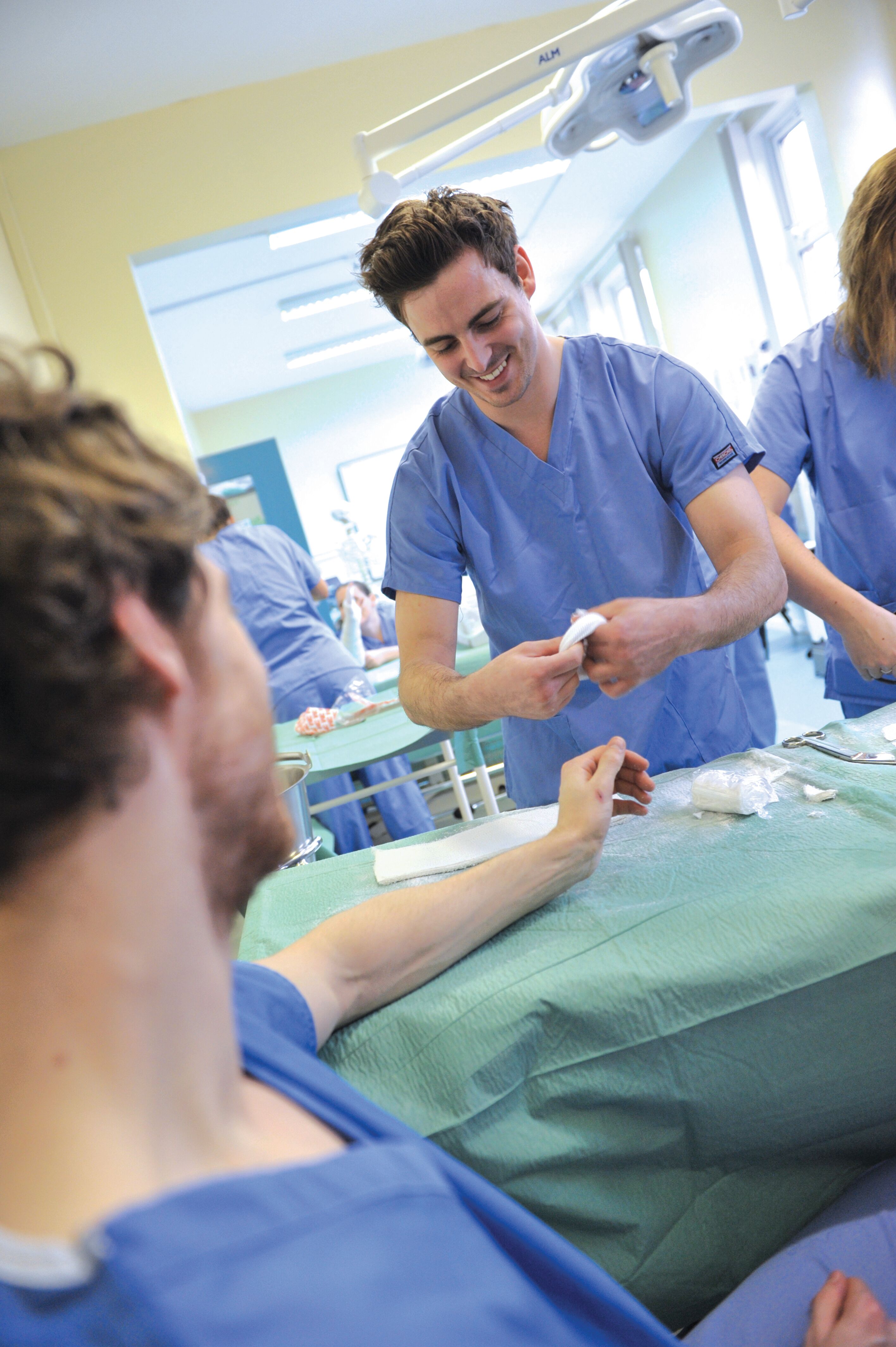 A male student nurse in blue scrubs practises plastering an arm