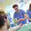 A male student nurse in blue scrubs practises plastering an arm
