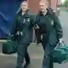 Two female student paramedics in green NHS uniform carrying equipment