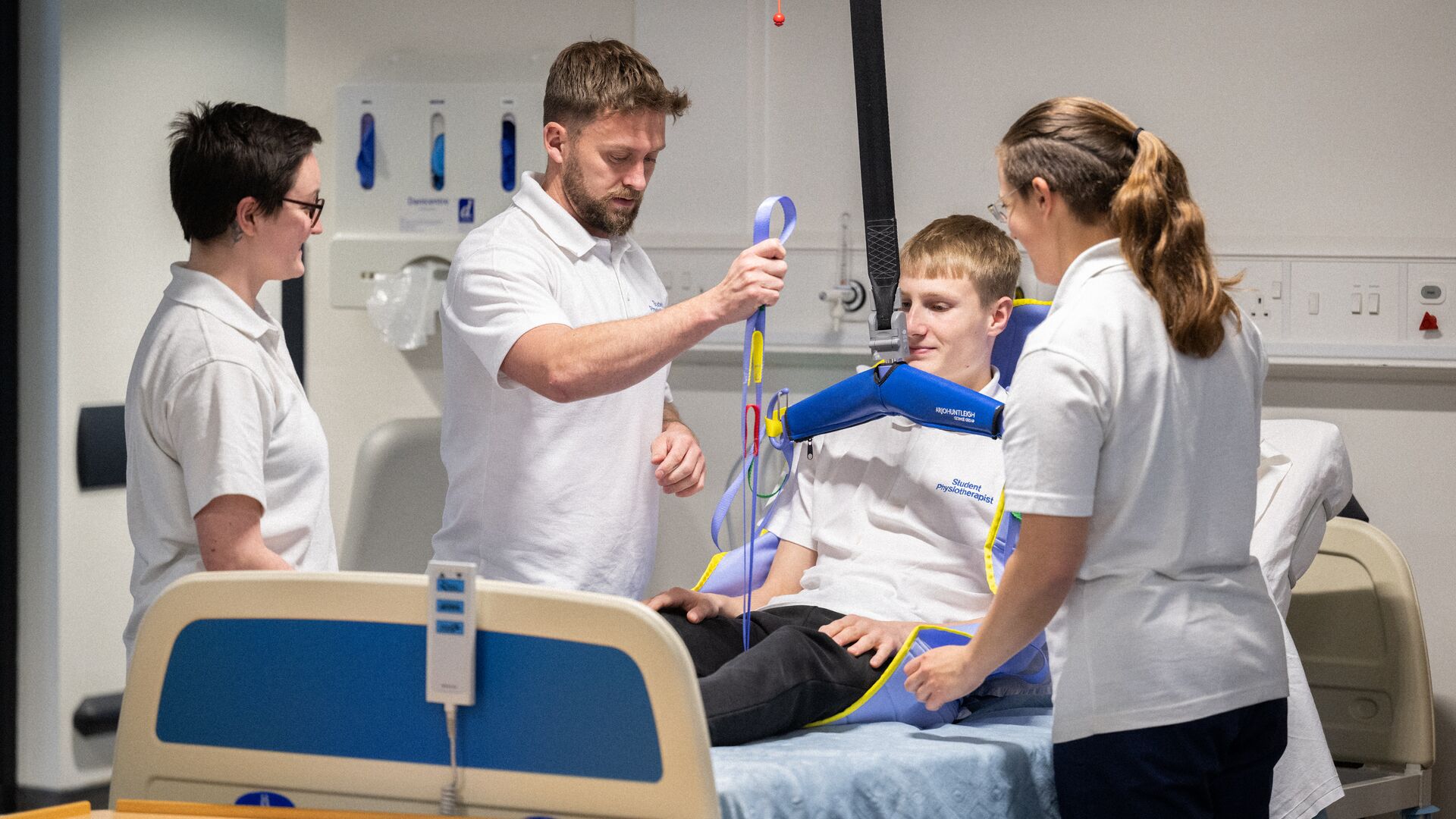 Three students stood around a physiotherapy patient in a hospital bed