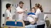 Three students stood around a physiotherapy patient in a hospital bed