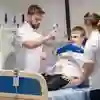 Three students stood around a physiotherapy patient in a hospital bed