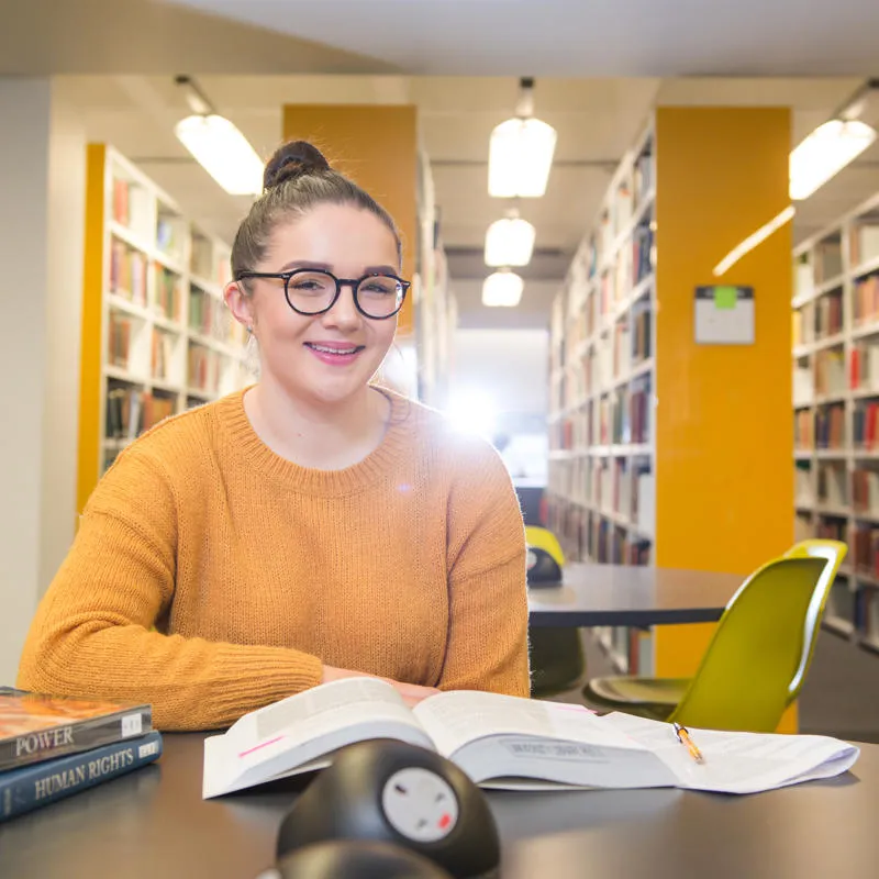 Student smiling on a table at the library