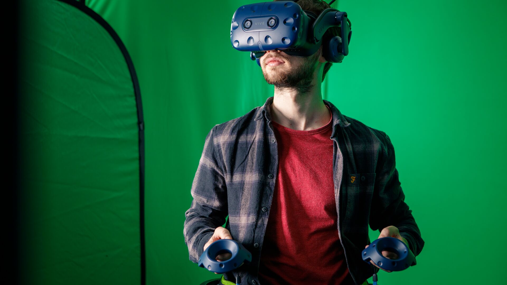 Game design student in a red t-shirt wearing a virtual reality headset in front of a green screen