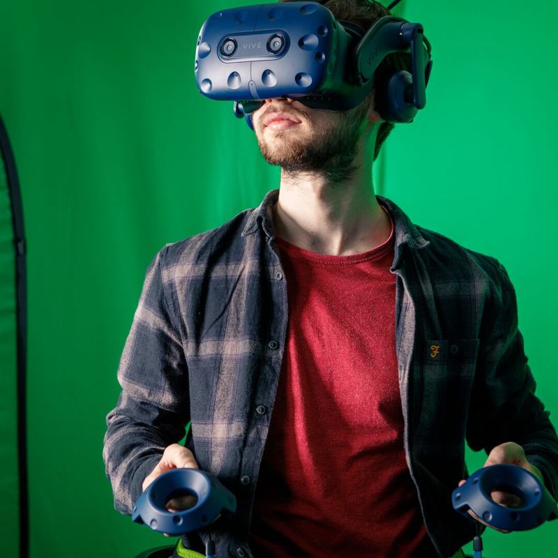 Game design student in a red t-shirt wearing a virtual reality headset in front of a green screen