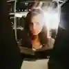 A female student with long dark hair reading a book as the camera looks at there through the shelf from the other side