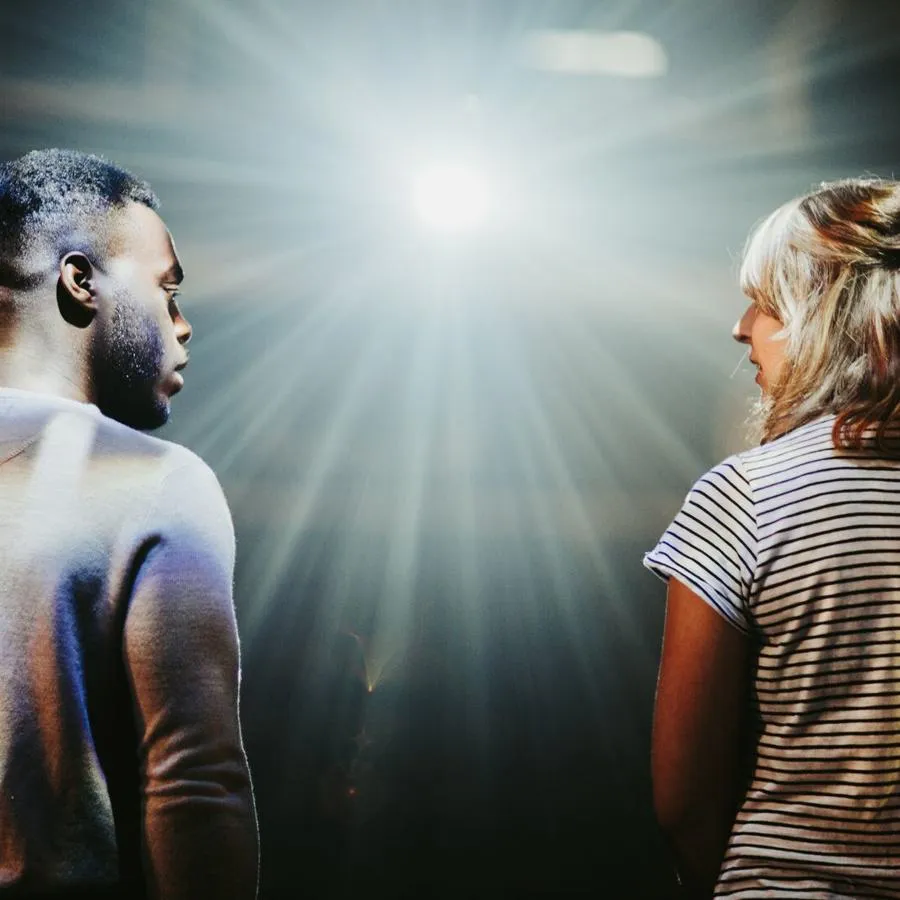 A young man and woman stand on stage with a bright light beaming down on them