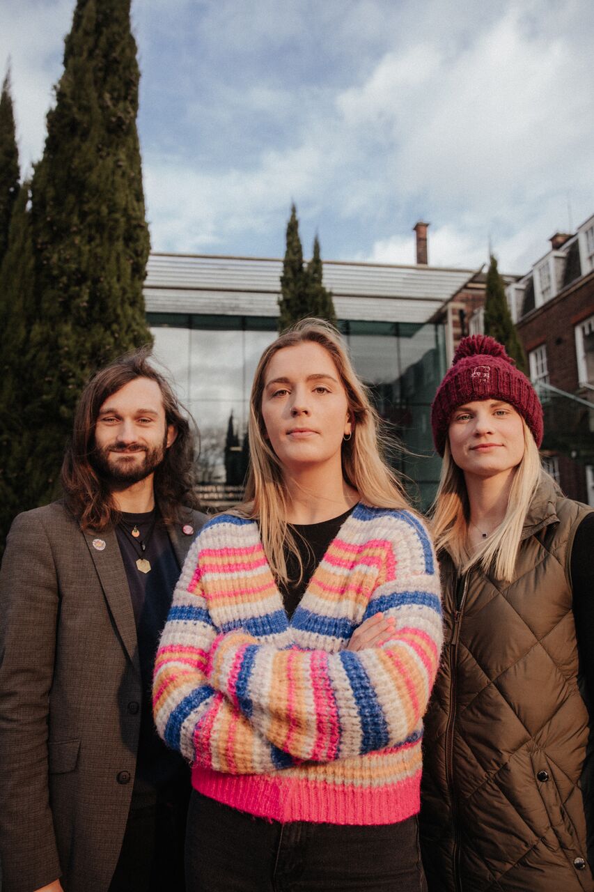 Three of Hull’s academics stand confidently together in front of ferns by the Business School's entrance