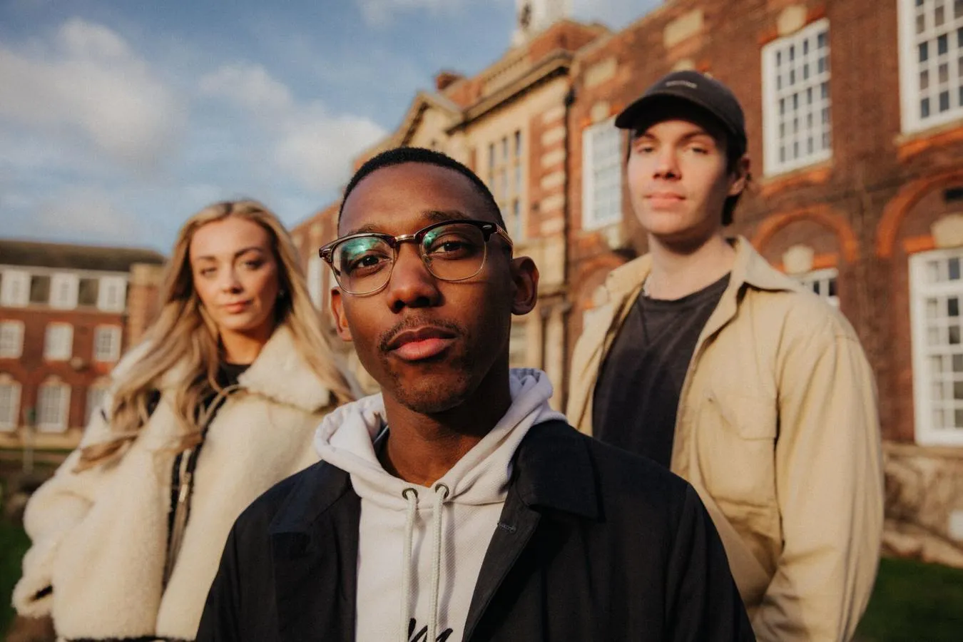 Three of Hull’s students stand confidently together on a lawn in front of beautiful red brick buildings