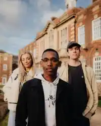 Three of Hull’s students stand confidently together on a lawn in front of beautiful red brick buildings
