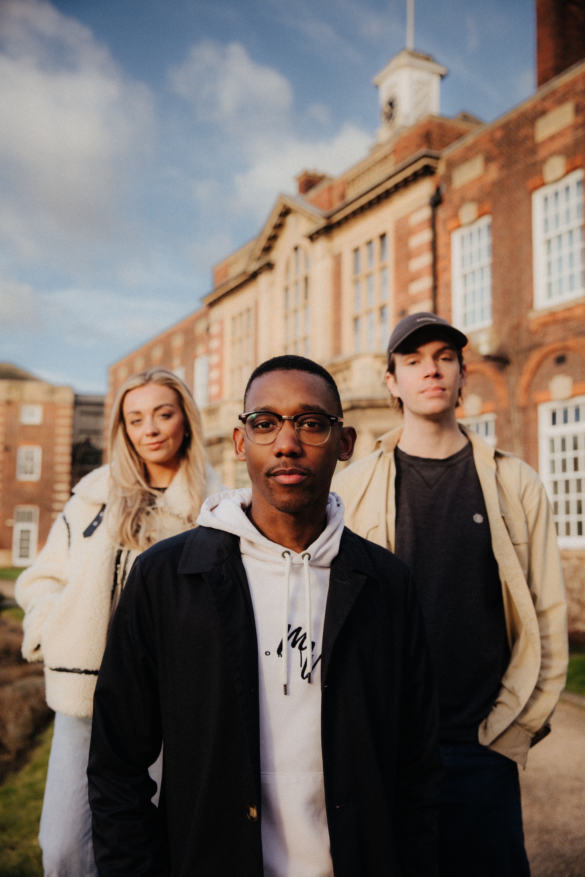 Three of Hull’s students stand confidently together on a lawn in front of beautiful red brick buildings