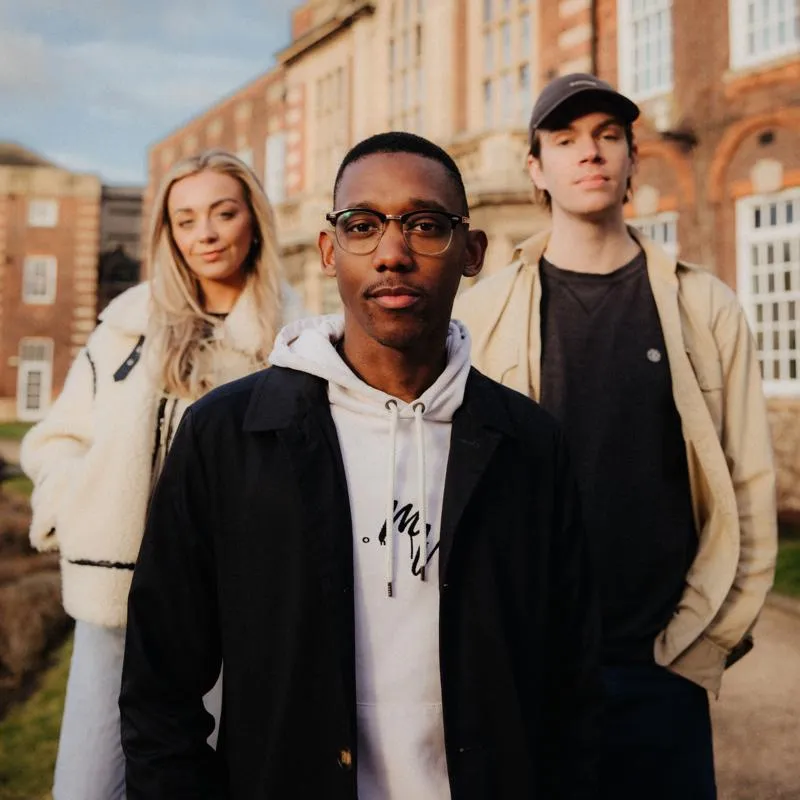 Three of Hull’s students stand confidently together on a lawn in front of beautiful red brick buildings