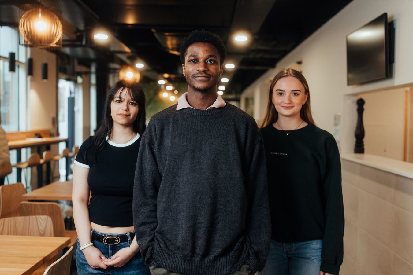 Three of Hull’s students stand confidently together under warm lighting in our pizzeria