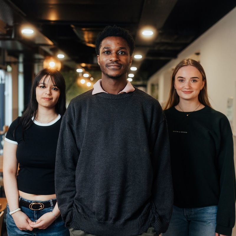 Three of Hull’s students stand confidently together under warm lighting in our pizzeria
