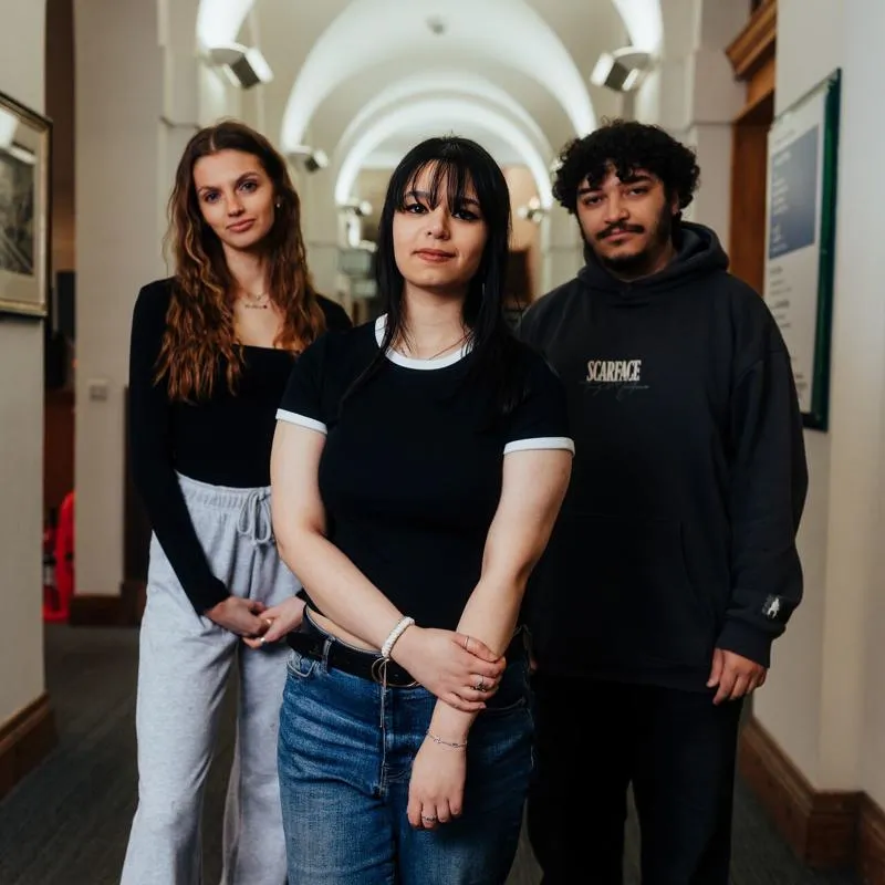 Three of Hull’s students stand confidently together in a brightly lit corridor in the business school