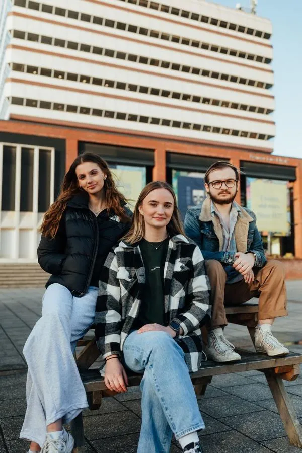 Three of Hull’s students sit confidently together on a picnic table in the Library Plaza