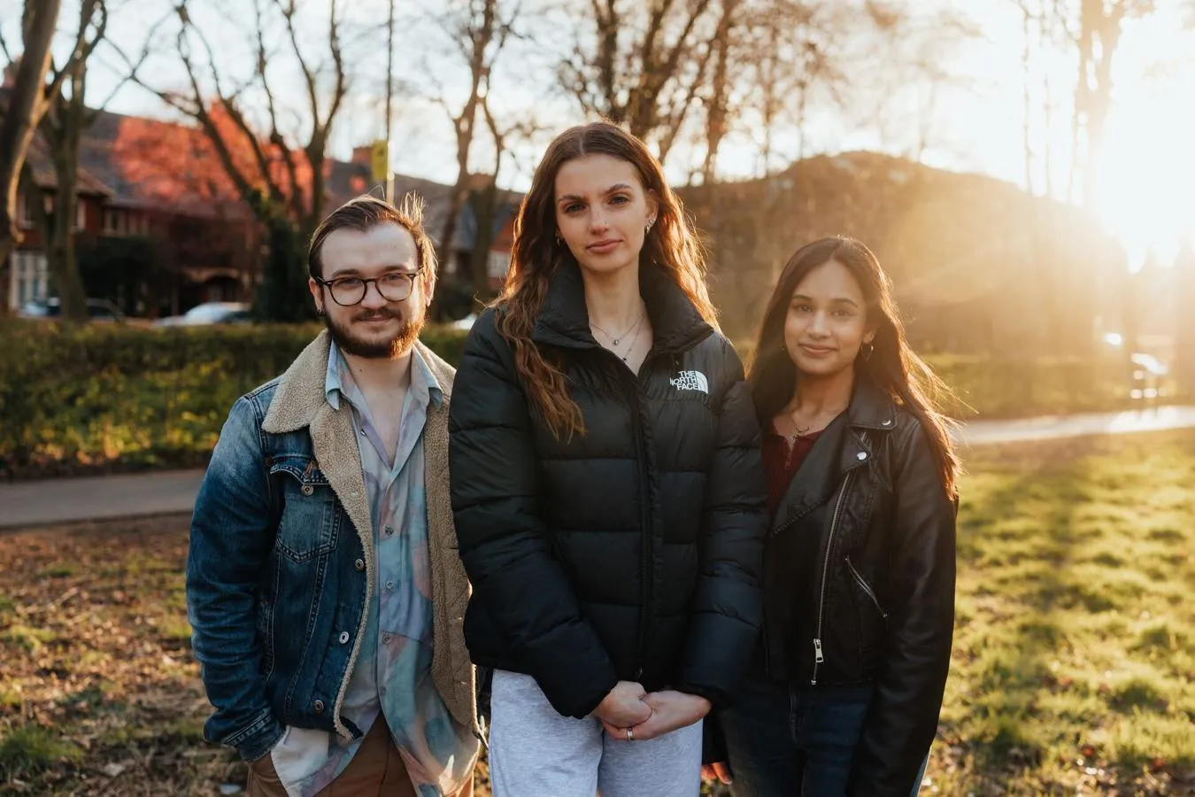 Three of Hull’s students stand confidently together under a setting sun in a wooded area of campus