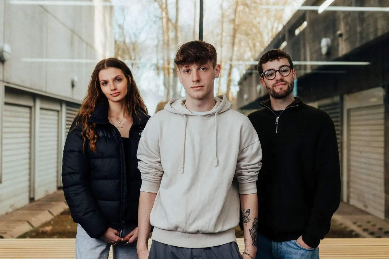 Three of Hull’s students stand confidently together in front of large glass windows in a teaching building