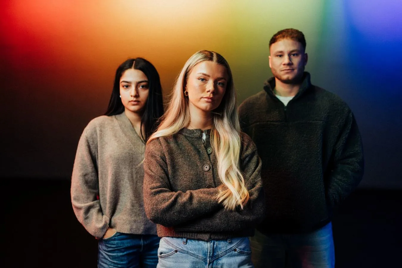Three of Hull’s students stand confidently together in front of multi-coloured lighting projected on to a back wall in Middleton Hall