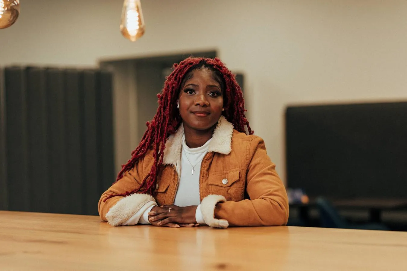 A female student sits at a desk underneath edison bulbs in a shared study area in the Library