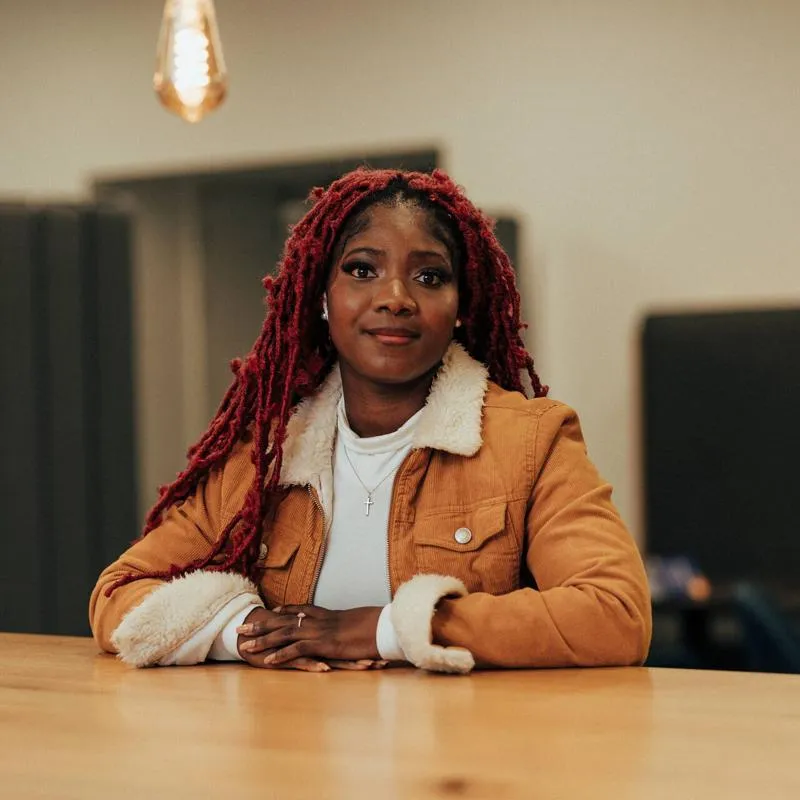 A female student sits at a desk underneath edison bulbs in a shared study area in the Library