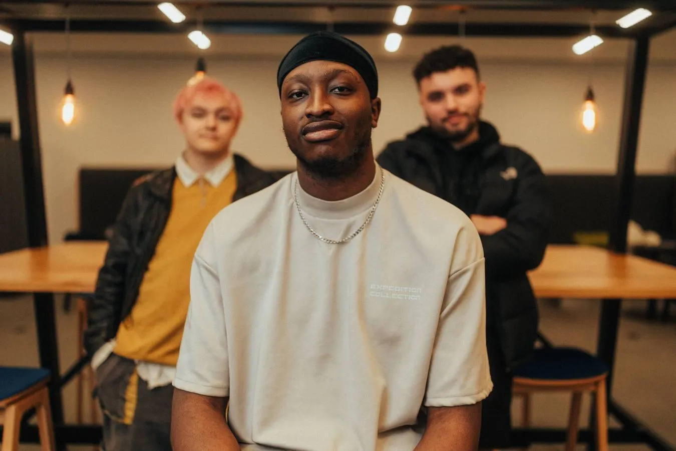 Three of Hull’s students sit and stand confidently together at a shared study area in the Library