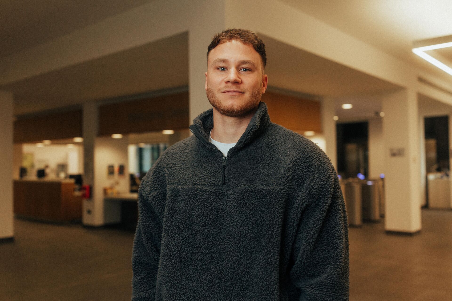 A male student in jeans and fleece stands confidently in front of the Library reception desk