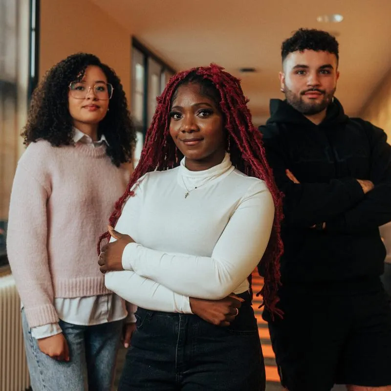 Three of Hull’s students stand confidently together in a modern corridor with wood panelling