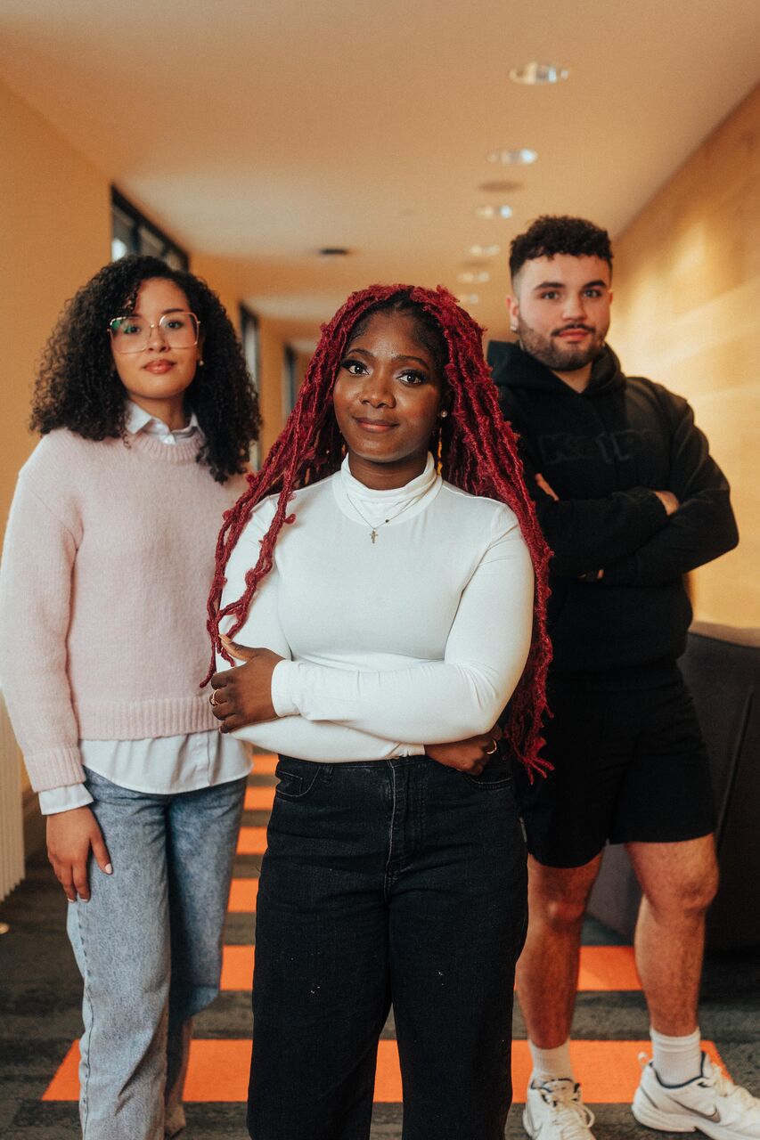 Three of Hull’s students stand confidently together in a modern corridor with wood panelling