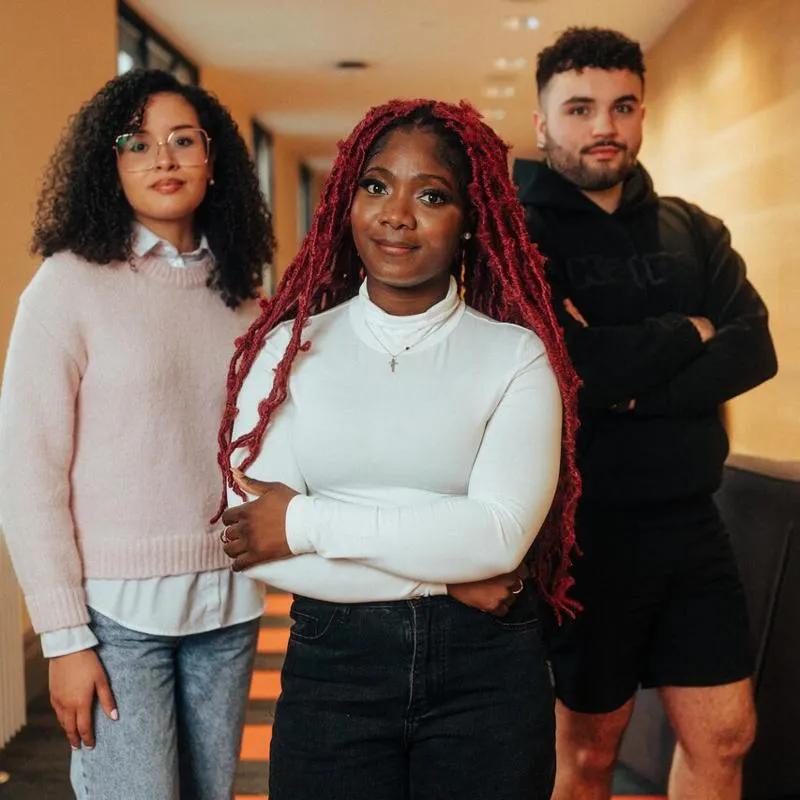 Three of Hull’s students stand confidently together in a modern corridor with wood panelling