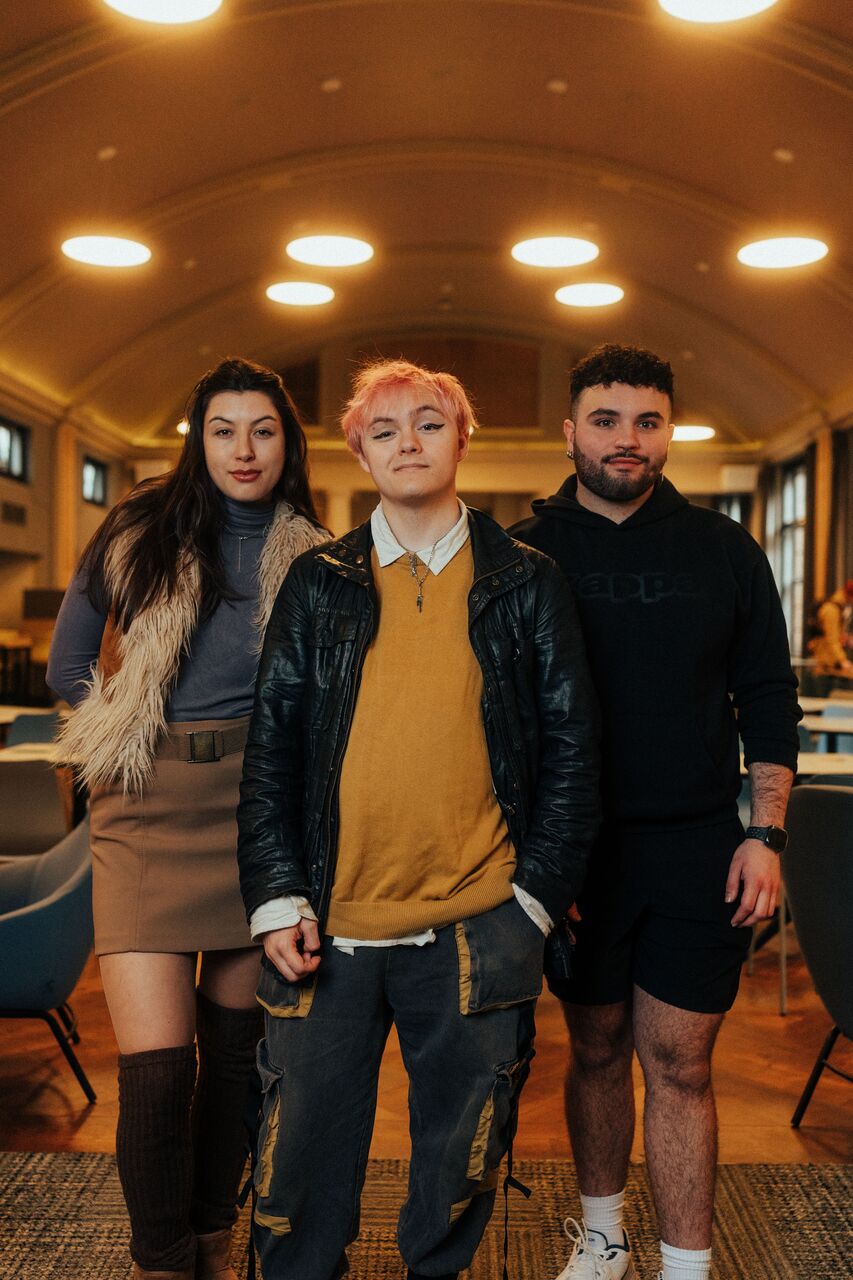Three of Hull’s students stand confidently together in a modern dining hall