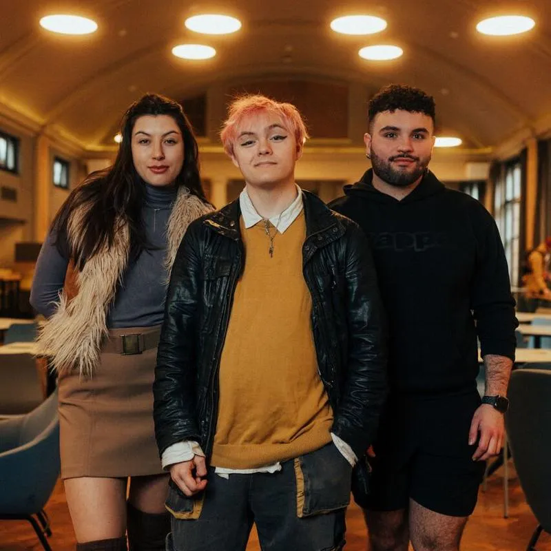 Three of Hull’s students stand confidently together in a modern dining hall