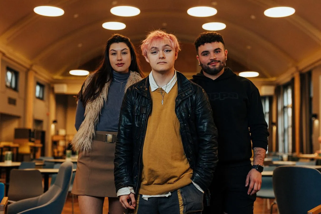 Three of Hull’s students stand confidently together in a modern dining hall