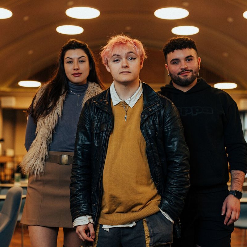 Three of Hull’s students stand confidently together in a modern dining hall