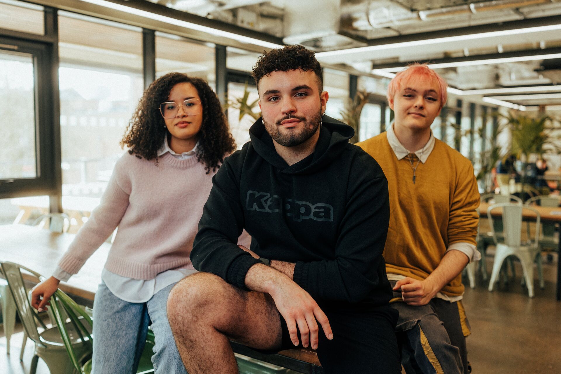 Three of Hull’s students sit confidently together in front of modern lighting and foliage in the student hangout
