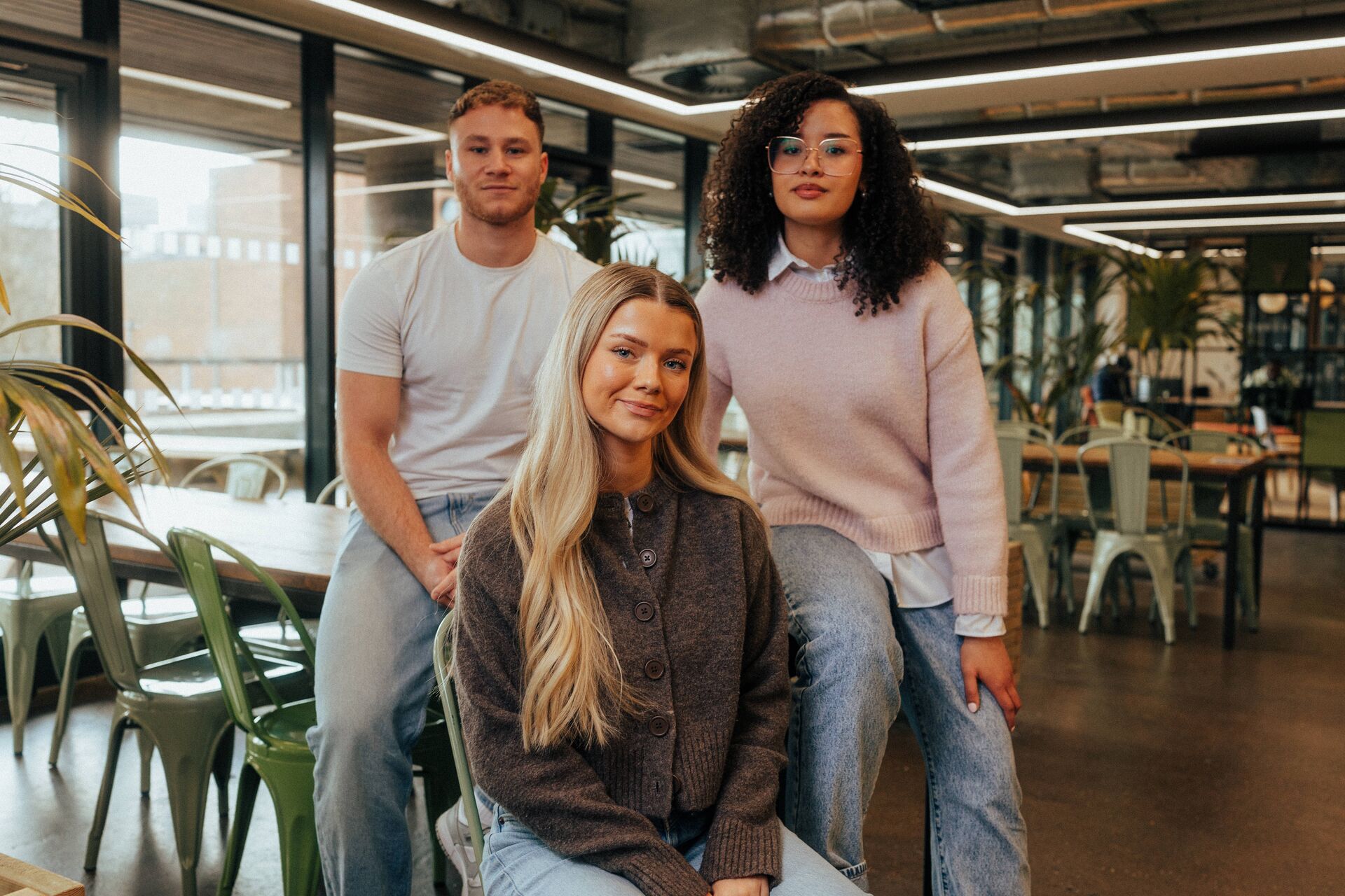 Three of Hull’s students sit confidently together in front of modern lighting and foliage in the student hangout