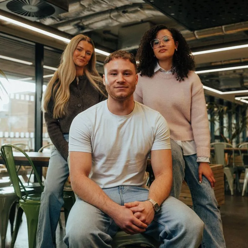 Three of Hull’s students sit confidently together in front of modern lighting and foliage in the student hangout