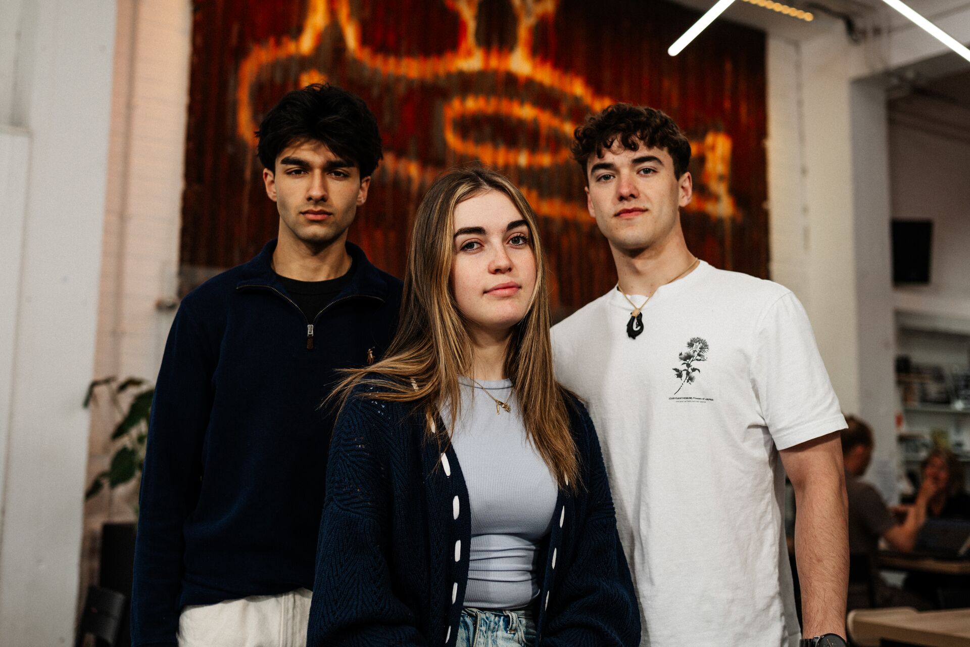 Three of Hull’s students stand confidently together in front of a rusted panel with Hull's iconic 'Dead Bod' artwork
