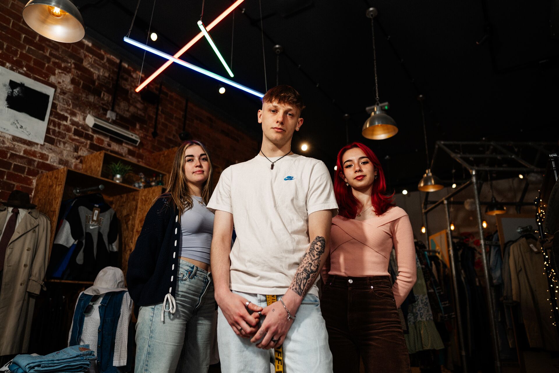 Three of Hull’s students stand confidently together under multicoloured strip lighting in a vintage clothes shop
