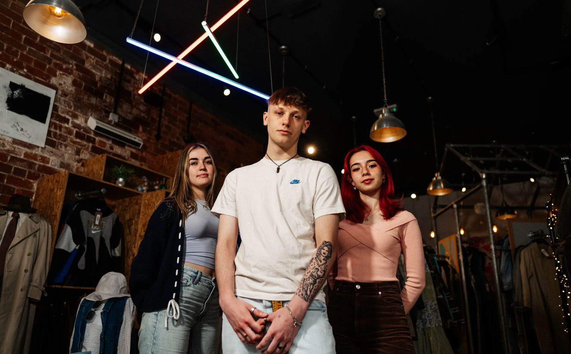 Three of Hull’s students stand confidently together under multicoloured strip lighting in a vintage clothes shop