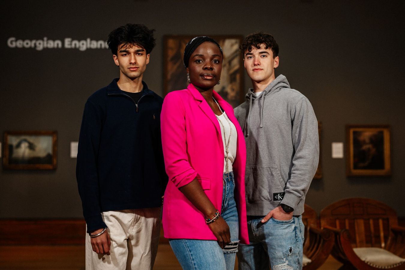 Three of Hull’s students stand confidently together in a dark gallery with Georgian paintings in Ferens Art Gallery