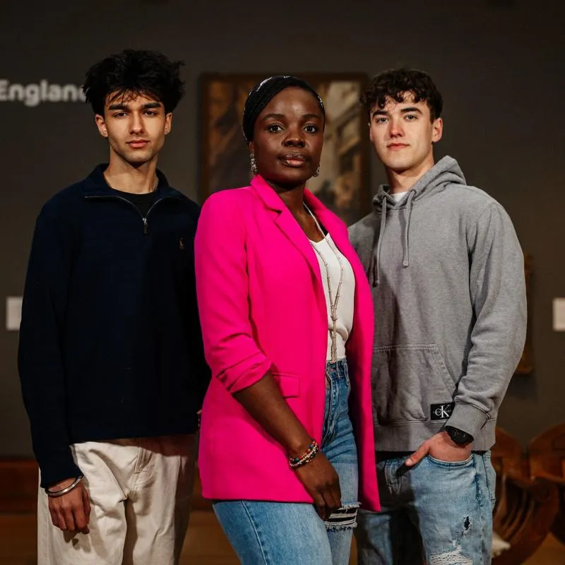 Three of Hull’s students stand confidently together in a dark gallery with Georgian paintings in Ferens Art Gallery