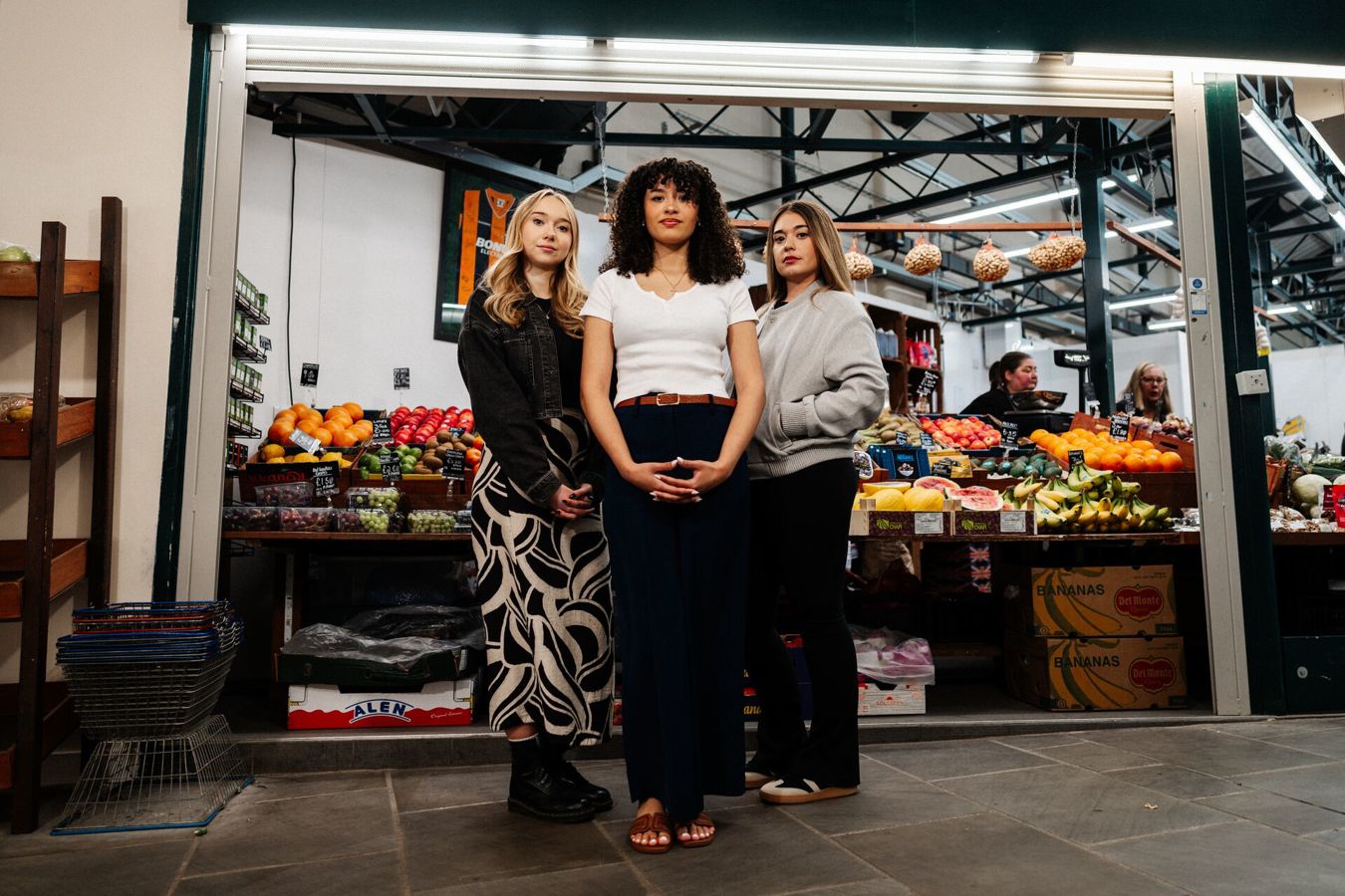 Three of Hull’s students stand confidently together in front of a fruit and veg stall in Hull's Trinity Market