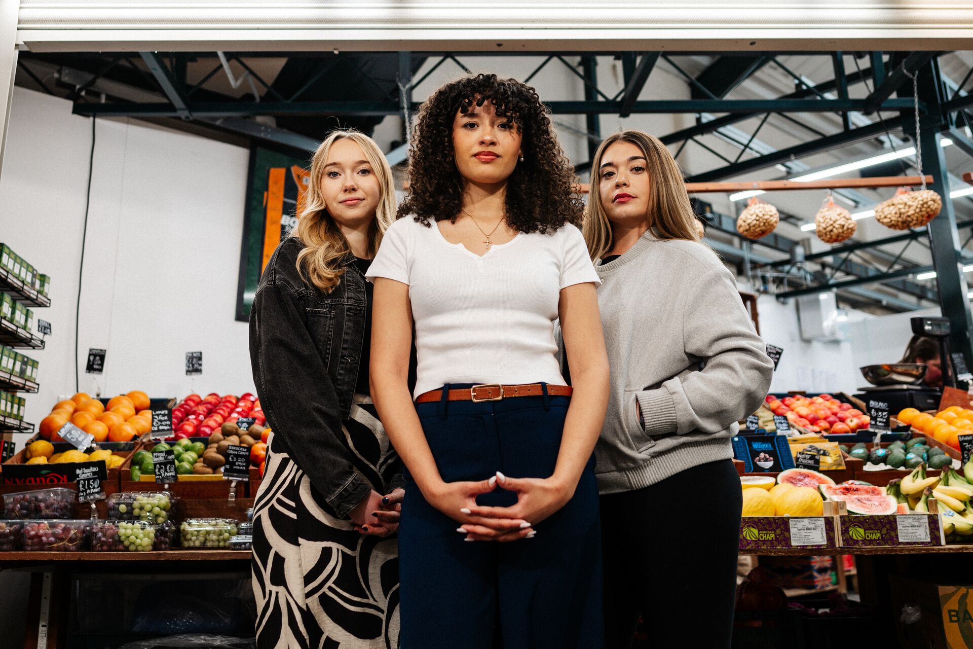 Three of Hull’s students stand confidently together in front of a fruit and veg stall in Hull's Trinity Market