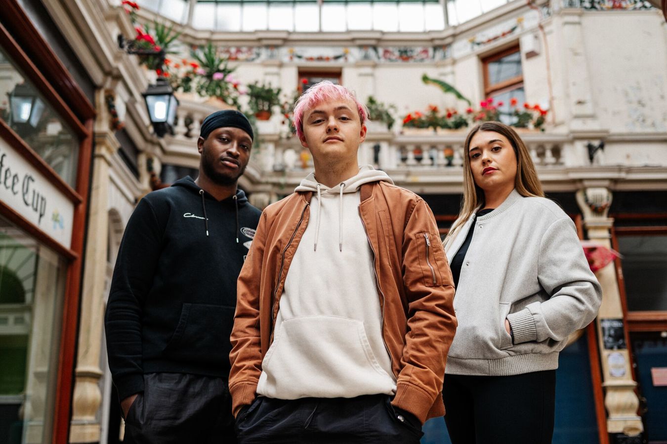 Three of Hull’s students stand confidently together in a beautiful shopping arcade with glass roof and flowers