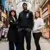 Three of Hull’s students stand confidently together in a beautiful shopping arcade with glass roof and flowers